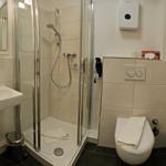 Badezimmer mit Dusche, Waschbecken und WC. Fliesen und weiße sanitäre Einrichtung.