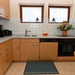 Kitchen with wooden cabinets, sink, stove, and microwave. Two windows with white curtains.