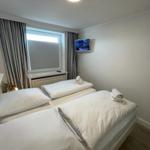 Room with two beds, window with blinds, and wall-mounted TV.