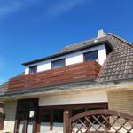 Haus mit Balkon, Dach und Terrasse unter blauem Himmel.