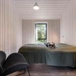 Schlafzimmer mit Bett, Fenster und grauer Sitzgelegenheit. Holzwandverkleidung und Regal.