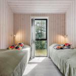 Zwei Betten mit bunten Kissen stehen in einem Raum mit Holzwandverkleidung und einem Fenster.