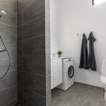 Badezimmer mit Dusche, Waschmaschine und Toilette. Graue Fliesen und weiße Wände.