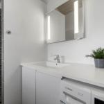 Badezimmer mit Waschbecken, Spiegel und Dusche. Unter dem Waschtisch steht eine Waschmaschine.
