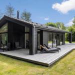 Moderne Villa mit Holzterrasse, Liegestühlen und Garten. Große Glasfronten und dunkle Holzfassade.