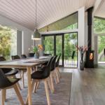 Essbereich mit Tisch, Stühlen und Blick auf Garten. Kamin und Sitzgelegenheit im Hintergrund.