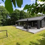 Ein modernes Haus mit Terrasse, Grill und Fußballtor auf grünem Rasen.