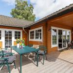 Holzhaus mit überdachter Terrasse, Tisch und Stühle. Blick auf Garten und Himmel.