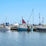 Fischerboote liegen im Hafen. Ein Boot hat eine rote Segel.