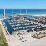Hafen mit Booten, Windkraftanlagen und Wohnhäusern an der Küste.
