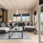 Ein Wohnzimmer mit grauem Sofa, Holzwänden und einer Terrasse.