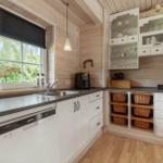 Küche mit Holzwänden, weißen Schränken und Fenster mit Blick auf Grün.