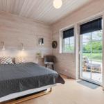 Schlafzimmer mit Bett, Fenstern und Balkontür. Holzwände und Boden.