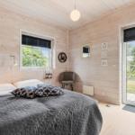 Schlafzimmer mit Holzwand, Bett, Fenster und Glastür zum Garten.