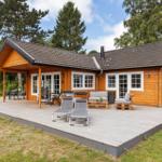 Holzhaus mit Terrasse, Liegestühlen und Garten. Fenster und Türen sind weiß.