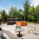 Terrasse mit Sitzgelegenheiten, Whirlpool und Holzsauna im Wald.