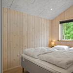 Schlafzimmer mit Holzwand, Bett und Fenster zum Wald