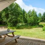 Terrasse mit Holztisch und Blick auf grüne Wiese und Wald.