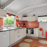Küche mit weißen Schränken, roter Mosaikwand und Terrakottaboden