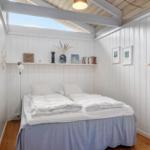 Schlafzimmer mit Doppelbett, weißen Wänden und Holzboden. Deckenfenster und Regal mit Dekor.