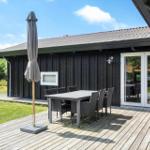 Terrasse mit Tisch, Stühlen und geschlossenem Sonnenschirm vor einem Holzhaus.