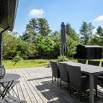 Holzterrasse mit Tisch, Stühlen und Sonnenschirm. Grünfläche und Bäume im Hintergrund.