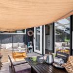 Terrasse mit Sitzgruppe, Tisch und Sonnensegel. Durchgehendes Glas verbindet Außen- und Innenbereich.