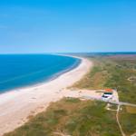 Aerielansicht einer Küstenlandschaft mit Strand, Meer und grünen Dünen.