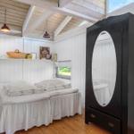 Schlafzimmer mit Doppelbett, schwarzer Kommode und Holzboden. Weiße Wände und hölzerne Decke.