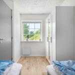 Zimmer mit zwei Betten, Fenster mit Blick auf Grün, weißer Schrank und Holzboden.
