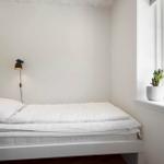 Schlafzimmer mit weißem Bett, Wandlampe und Pflanzen am Fenster.