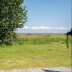 Von der Terrasse aus Blick auf grünes Gras und einen Wald. Im Hintergrund ist ein Fluss mit blauem Himmel zu sehen.