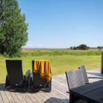 Terrasse mit Loungemöbeln und Blick auf grünes Feld unter blauem Himmel.