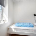 Schlafzimmer mit Bett, Fenster und Pflanze. Wandlampe und weißer Rahmen.