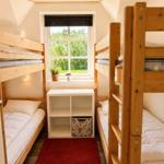 Zimmer mit zwei Holzbetten, Fenster und kleinem Regal.