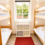 Zwei Etagenbetten, ein Fenster, ein weißer Schrank und ein roter Teppich.