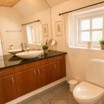Badezimmer mit Waschtisch, Spiegel und Toilette. Fenster mit Pflanze und Vorhang.