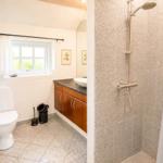 Badezimmer mit Dusche, Toilette und Waschbecken unter Fenster.