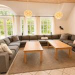 Großer Wohnbereich mit L-förmigem Sofa, zwei Holztischen und großen Fenstern.