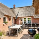 Terrasse mit Tisch, Stühlen und Grill unter strohgedecktem Dach.