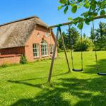 Haus mit Strohdach und Spielplatz mit Schaukel im Garten.