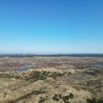 Weitläufige Landschaft mit Mooren und Wasserflächen unter blauem Himmel.