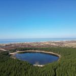 Ein See im Wald mit Blick auf das Meer und Hügel