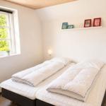 Zimmer mit Doppelbett, Fenster mit Blick auf Grün und Wandregal mit Bilderrahmen.
