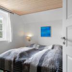Schlafzimmer mit Bett, Fenster und Wandbild. Holzdecke und weiße Wände.