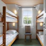 Zimmer mit zwei Doppelstockbetten, Stuhl und Fenster mit Blick auf Grün.