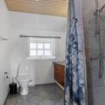 Badezimmer mit Dusche, Toilette und Fenster. Holzdecke und graue Fliesen.