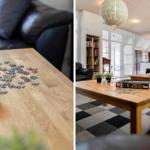 Ein Wohnzimmer mit Holztisch, Puzzle und schwarzen Ledersofas. Zwei runde Lampen hängen von der Decke.