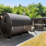 Holzsauna mit Dach und Tür. Nebenher Whirlpool und Sitzbereich im Garten.