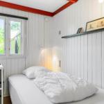 Ein Schlafzimmer mit weißer Holzwand, Bett, Fenster und Regal.